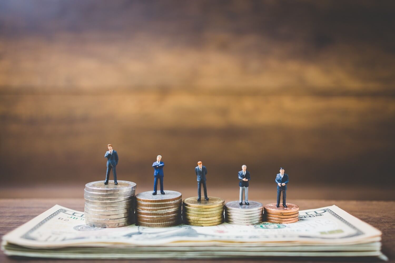 Miniature businessman figures standing stacks coins over dollar billst